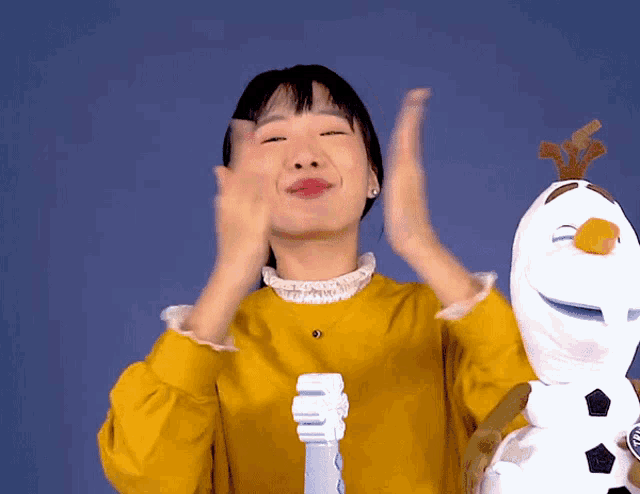 a girl in a yellow sweater is holding a toothbrush in front of an olaf stuffed animal