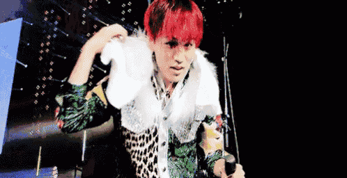 a man with red hair is standing on a stage holding a microphone and a fur collar .