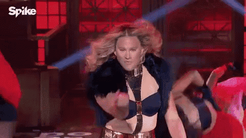 a woman in a fur coat is dancing on a stage with a spike logo in the background .