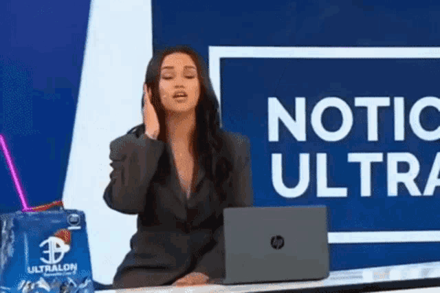 a woman in a suit is sitting at a desk with a laptop and talking on a cell phone .