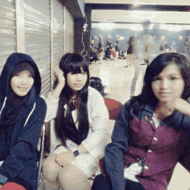 three young women are sitting next to each other in a room in front of a crowd .