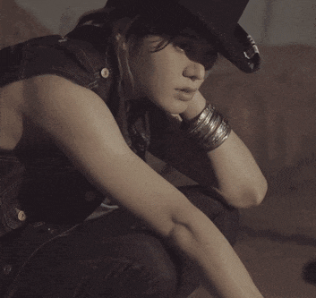 a woman wearing a cowboy hat and a denim vest is kneeling down