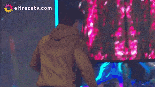 a man stands in front of a screen that says eltrecetv.com on the bottom
