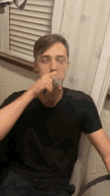a young man in a black shirt is brushing his teeth