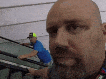 a bald man with a beard is riding an escalator while another man looks on .