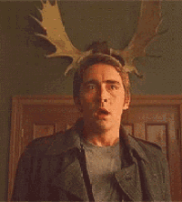 a man wearing a moose antlers headband has a surprised look on his face