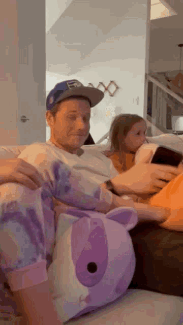 a man in a baseball cap is sitting on a couch with two children and a stuffed animal .