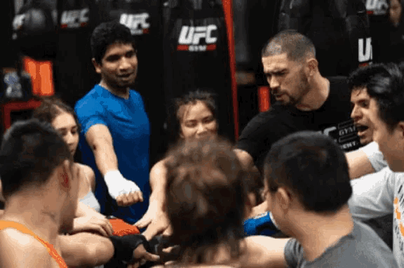 a group of people are gathered in a gym with ufc bags behind them