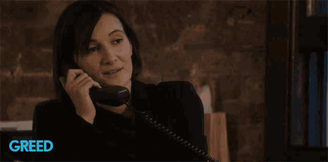 a woman is smiling while talking on a phone with greed written on the bottom right