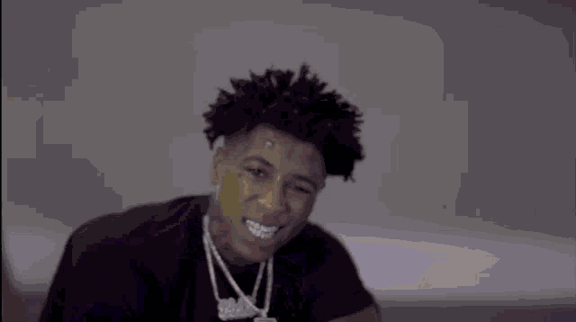 a young man wearing a black shirt and a necklace is making a face .
