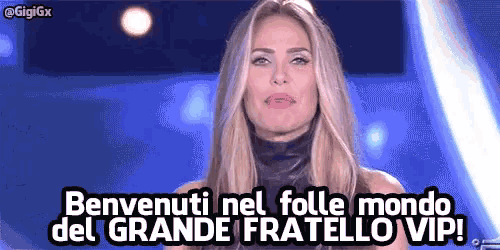 a woman is standing in front of a blue background and saying benvenuti nel folle mondo del grande fratello vip