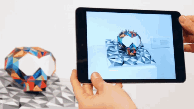 a person is holding a tablet with a picture of a colorful sculpture on the screen