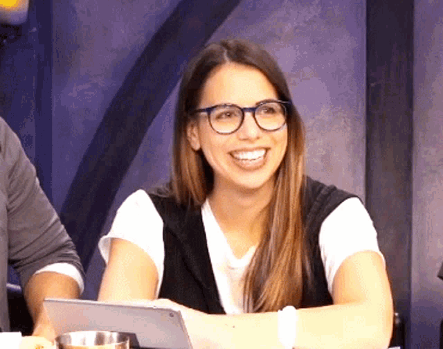 a woman wearing glasses smiles while sitting at a table