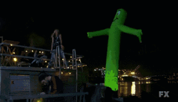 a woman is dancing in front of a green inflatable monster with fx written on it