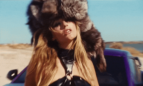a woman in a fur hat is standing next to a purple car