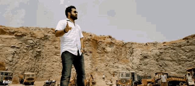 a man in a white shirt stands in front of a pile of rocks and trucks with the word myngiri on the bottom