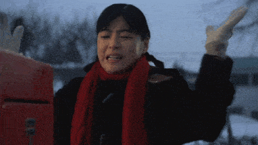 a woman wearing gloves and a red scarf is standing in front of a red mailbox
