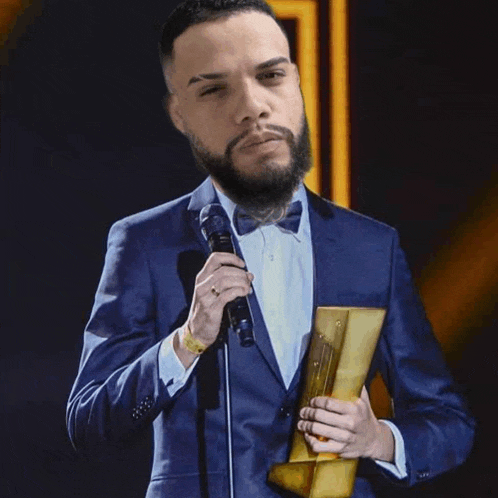 a man in a suit and bow tie holds a microphone and a trophy