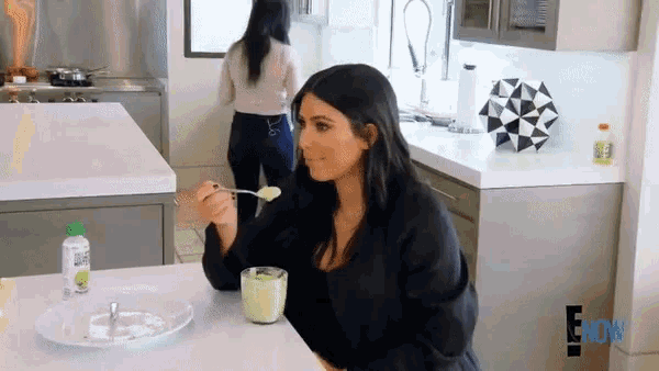 a woman is sitting at a table in a kitchen eating yogurt with a spoon .