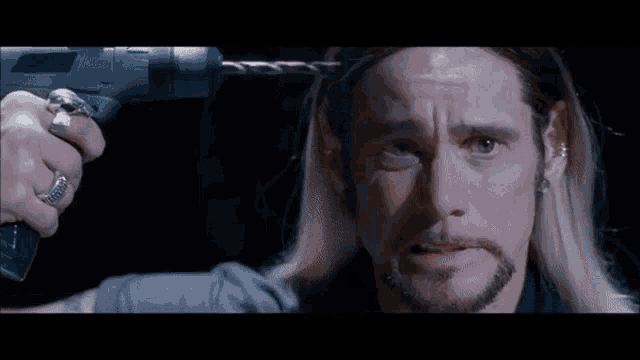 a man with long blonde hair and a beard is being shaved by another man