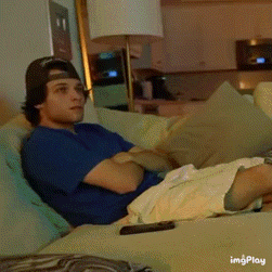 a man is laying on a couch with his arms crossed and a remote control in front of him