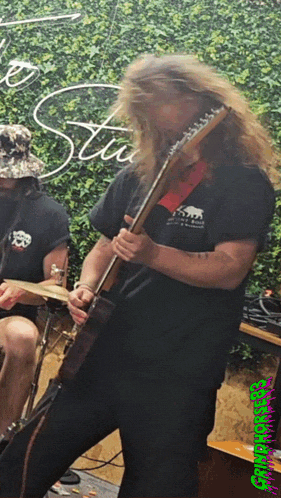 a man with long hair is playing a guitar in front of a sign that says stu