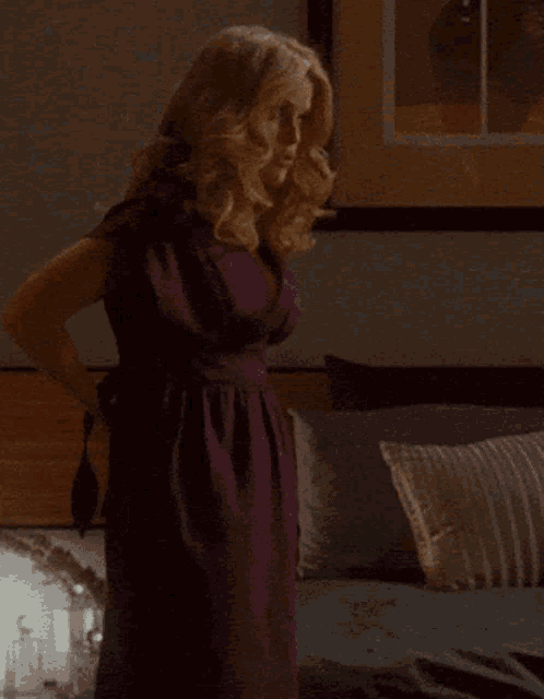 a woman in a purple dress is standing on a bed
