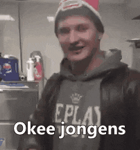 a man wearing a beanie and a hoodie is standing in front of a counter and says okee jongens .