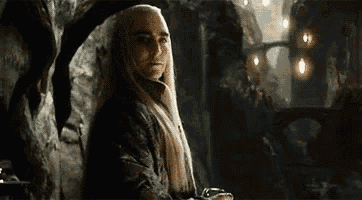 a man with long white hair is sitting in a chair in front of a cave .