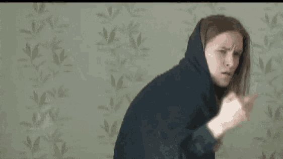 a woman in a hoodie is making a funny face and pointing at the camera .