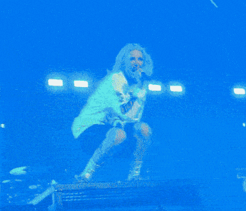 a woman in a yellow hoodie is singing into a microphone while squatting on a stage
