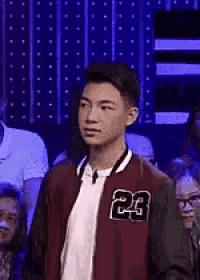 a young man wearing a bomber jacket with the number 23 on it is standing in front of a crowd .