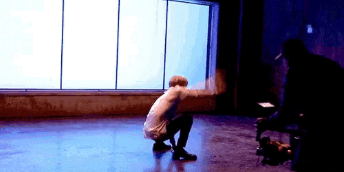 a man is squatting on the floor in front of a window in a room .