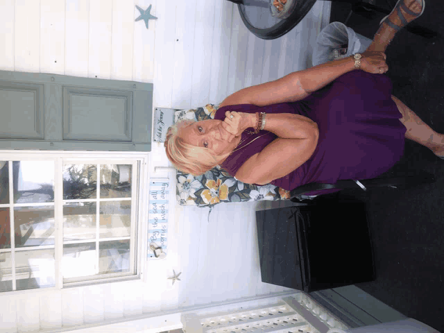 a woman in a purple dress sits on a porch with a sign that says to be yours on the wall behind her