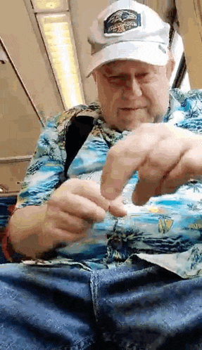 an elderly man wearing a hat and a hawaiian shirt is sitting on a train .