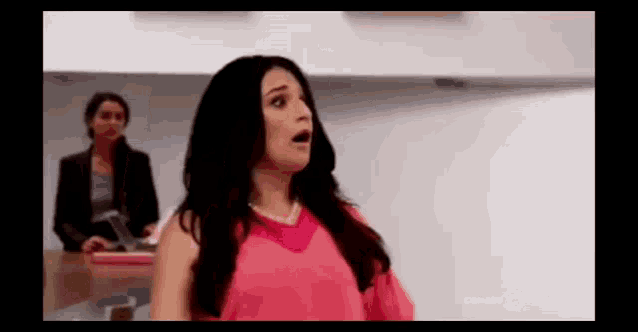 a woman in a pink dress is standing in front of a white wall and looking surprised .