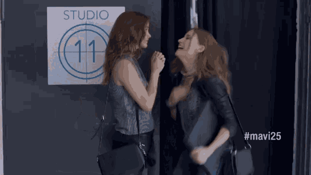 two women are standing in front of a studio 11 sign