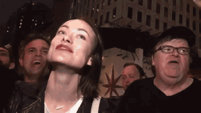 a group of people including a man with glasses and a woman with red lips looking up