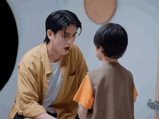 a man in a yellow shirt is talking to a little boy in a room .