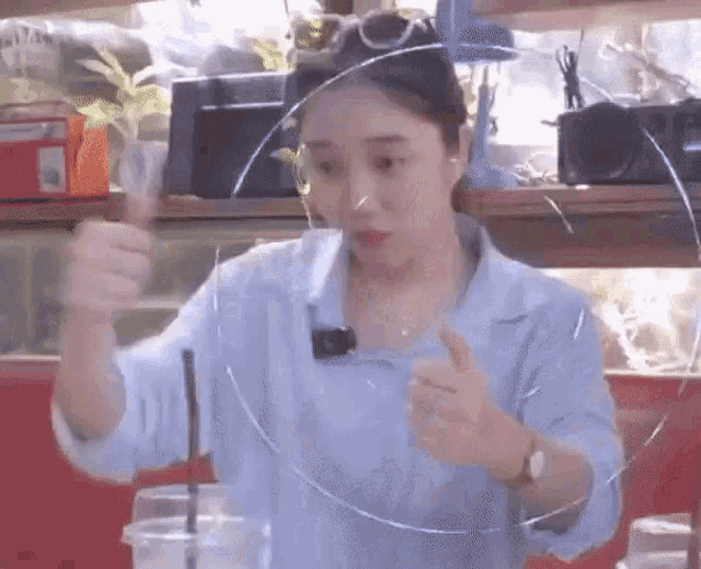 a woman in a blue shirt is holding a straw in her hand and making a funny face .