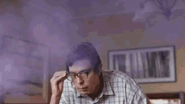 a man with glasses and purple smoke coming out of his head is sitting at a table .