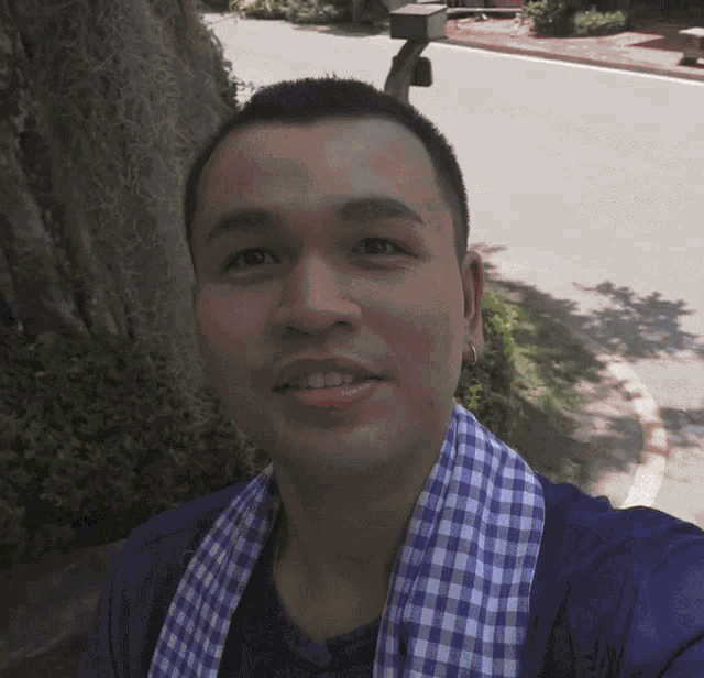 a man wearing a blue shirt and a blue and white plaid scarf smiles for the camera