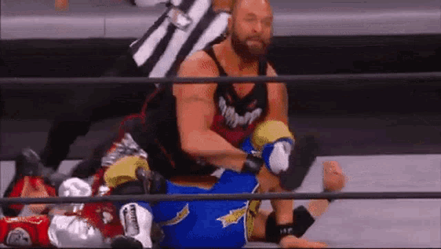 a man is wrestling another man in a ring with a referee in the background .