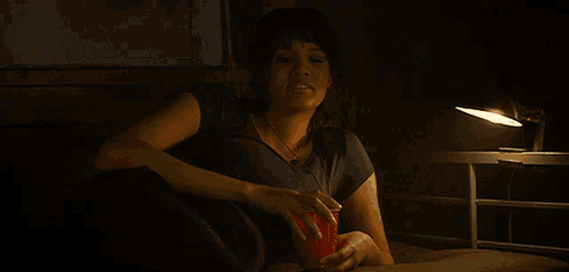 a woman sits on a bed with a red cup in her hand