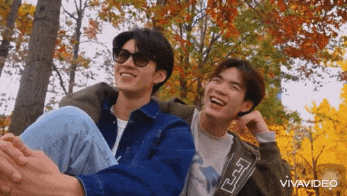 a couple of young men are sitting next to each other in a park and smiling .