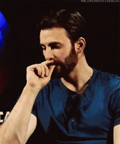 a man with a beard wearing a blue shirt is holding his hand to his mouth .