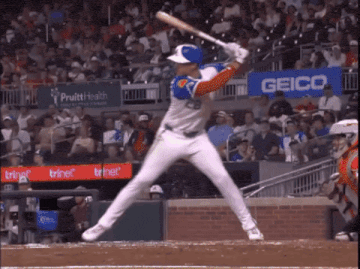 a baseball player getting ready to swing at a ball with a geico sign in the background