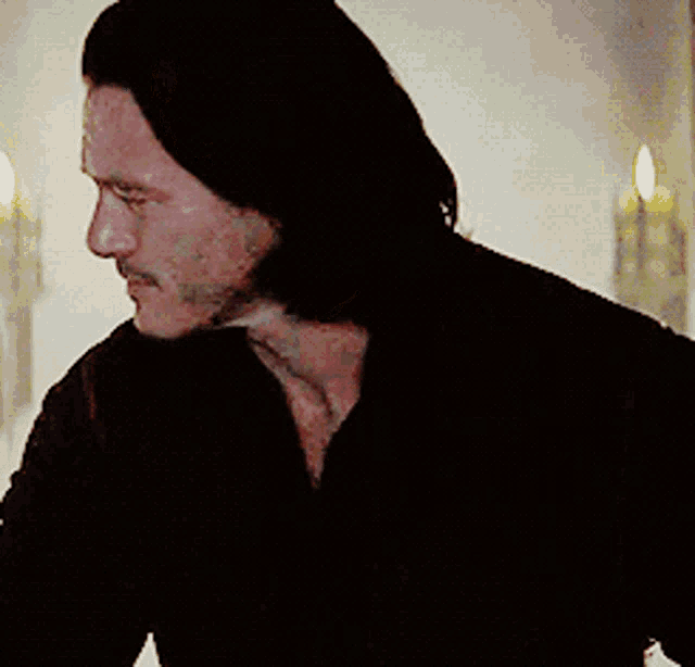 a man with long hair and a beard is wearing a black shirt and looking at the camera .