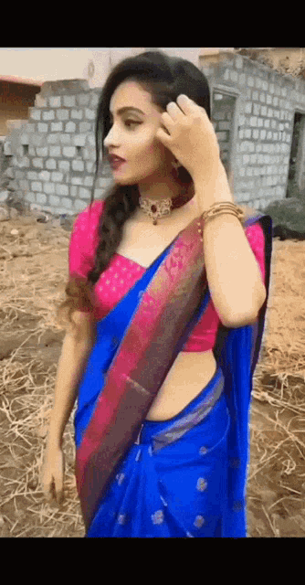 a woman in a blue saree and pink top is standing in a field .