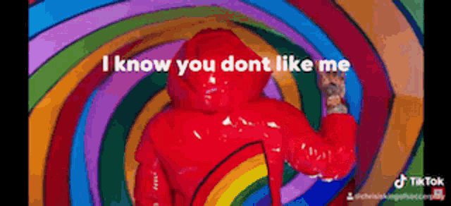 a man in a red rubber suit is surrounded by a rainbow and says i know you dont like me